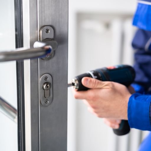 Técnico realizando cambio de chapa en puerta de cristal y aluminio con herramientas especializadas, servicio profesional de cambio de chapa.