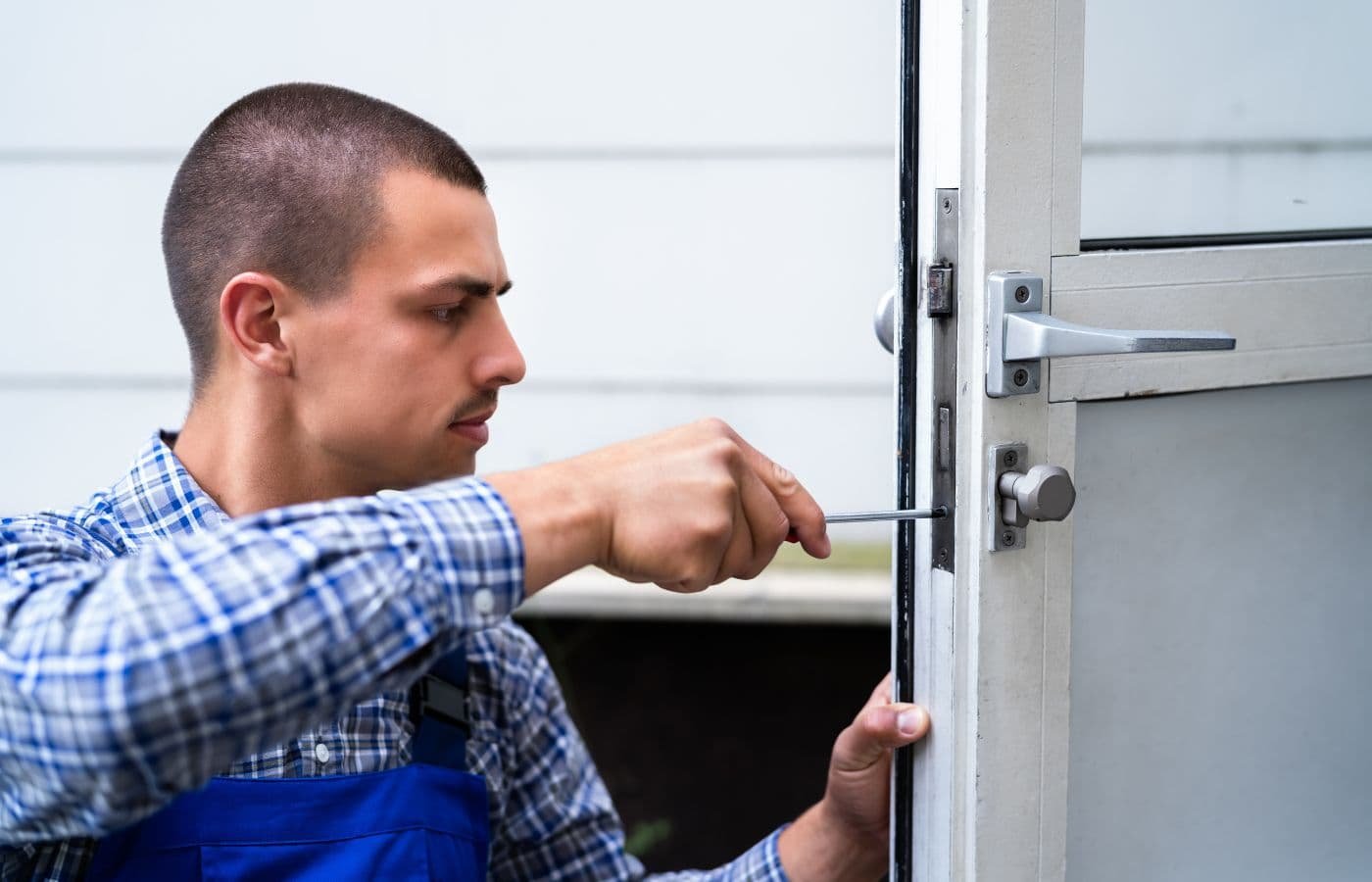 Cerrajero profesional realizando servicio de cerrajería residencial ajustando una cerradura en la puerta principal de una casa.