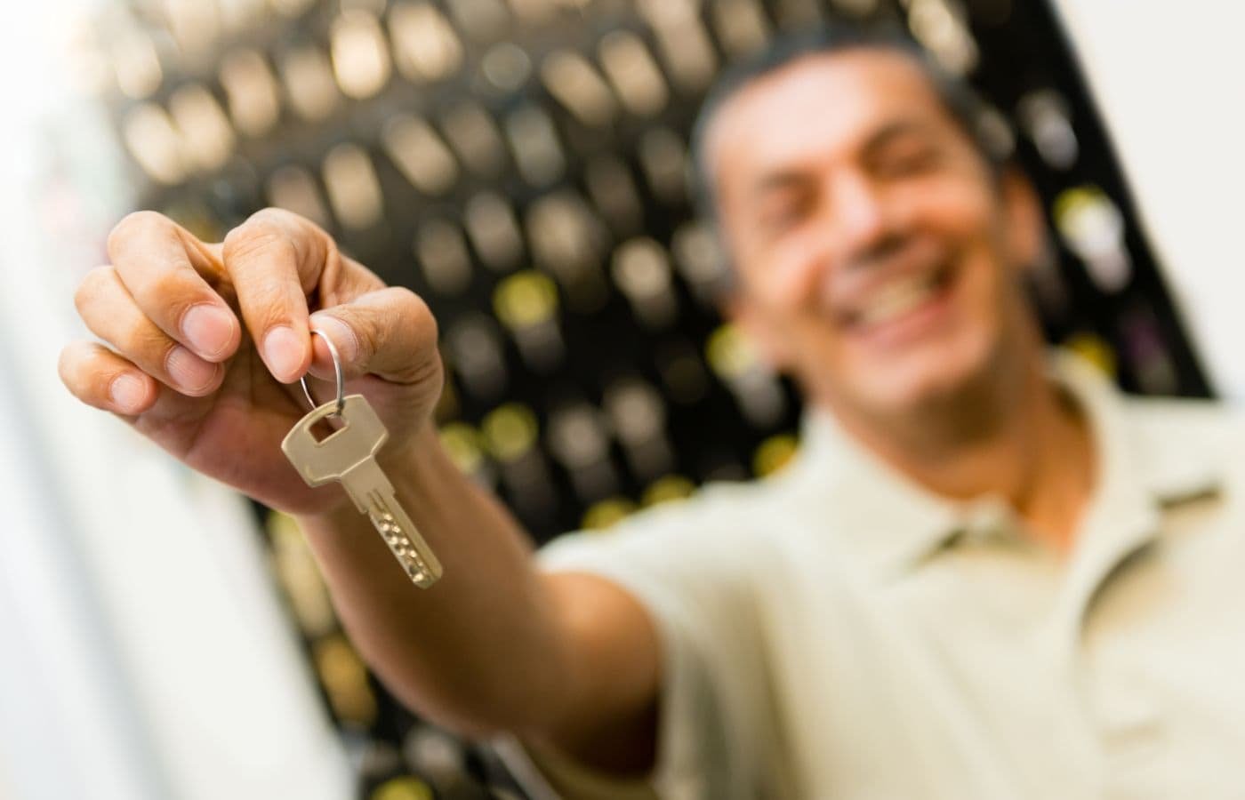 Cerrajero sonriente sosteniendo una llave en una cerrajería, con fondo de llaves colgadas. Servicio de cerrajería en Rosarito disponible 24/7.